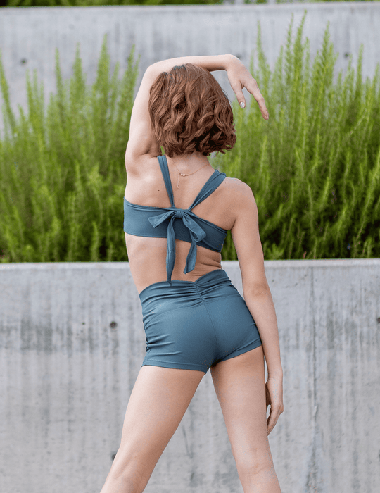 Woman wearing a blue bikini set with a concrete wall and greenery in the background