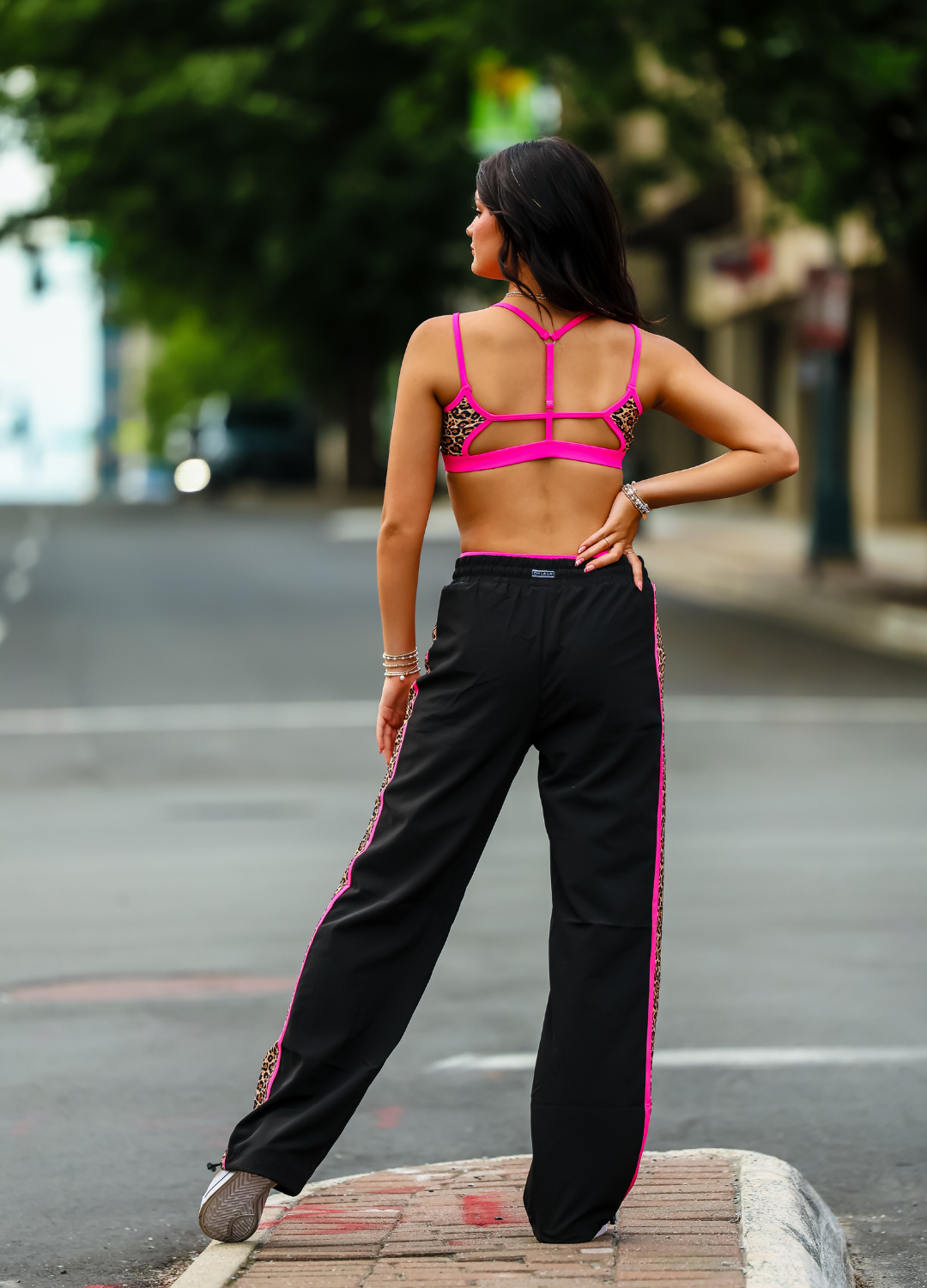 Woman wearing a bright pink sports bra and black pants with pink stripes on a street.