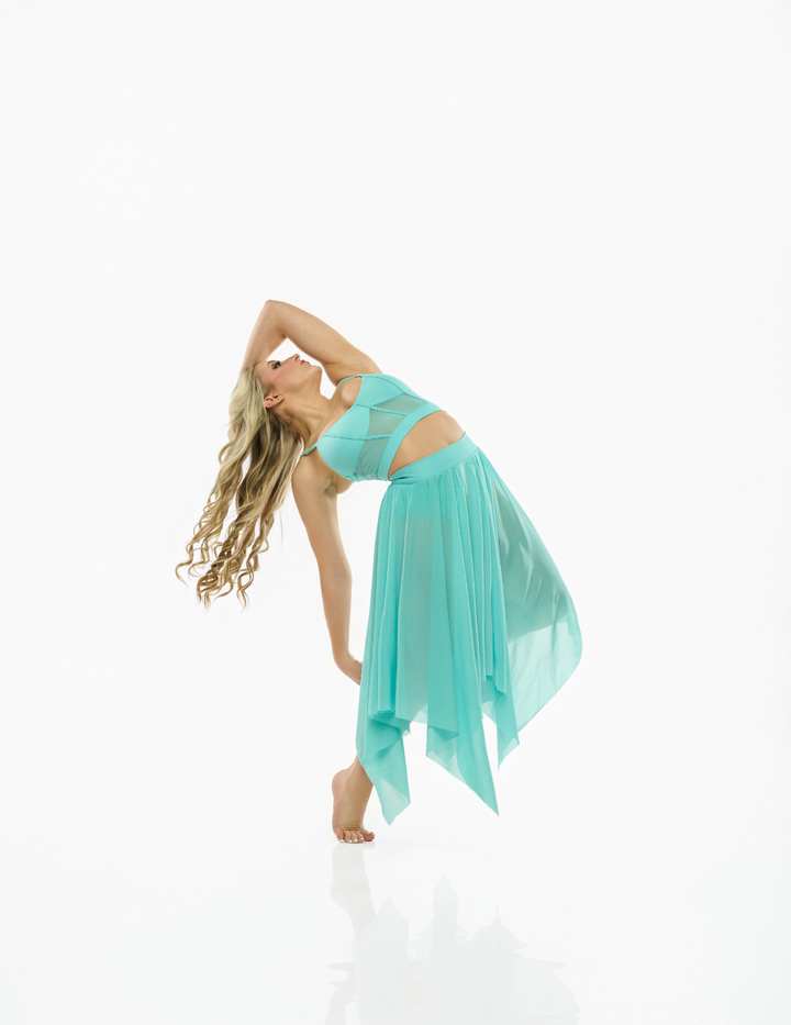A woman in a flowing mint green two-piece outfit with a sheer mesh crop top and a high-low pleated skirt, posing in a side stretch on a reflective white studio floor.