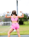 Person wearing pink athletic outfit flexing muscles outdoors