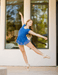 Dancer in a blue outfit practicing ballet outside a building with large windows.