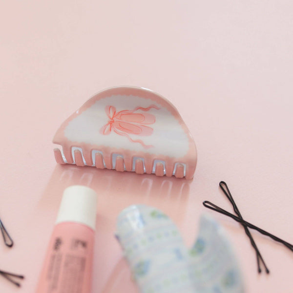 Hair styling tools including a hair roller, hairbrush, and hair clips on a pink background