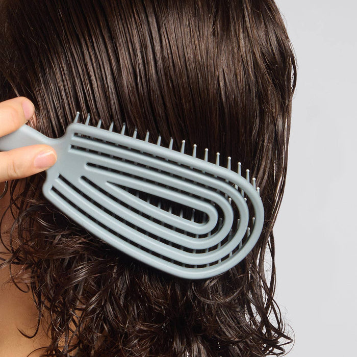 Person using a gray wide-tooth comb on wet hair against a neutral background