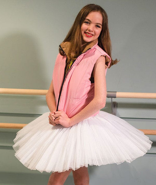 Young girl in a pink vest and white tutu standing in front of a ballet barre.