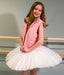 Young girl in a pink vest and white tutu standing in front of a ballet barre.