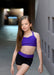 Young girl in a purple sports bra and black shorts standing against a neutral background