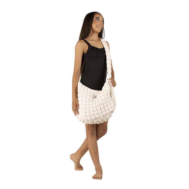 A woman modeling a chunky, quilted off-white shoulder bag against a solid white background.