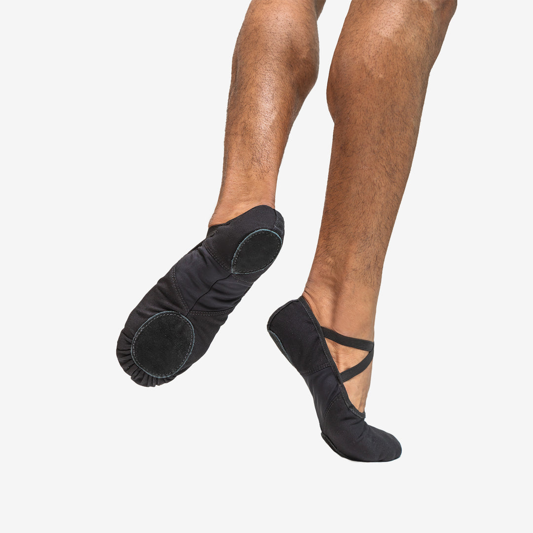 Black ballet shoes worn by a person on a white background