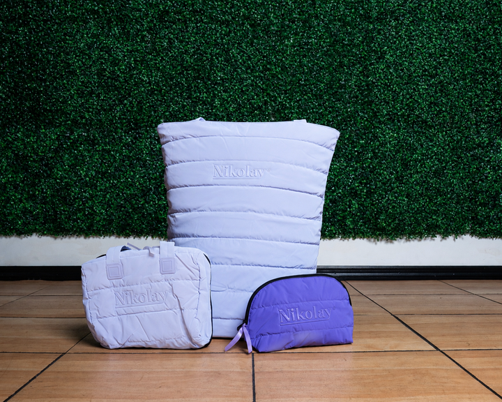 Three quilted bags in Lilac and Lavender on a wooden floor with a green textured wall background.