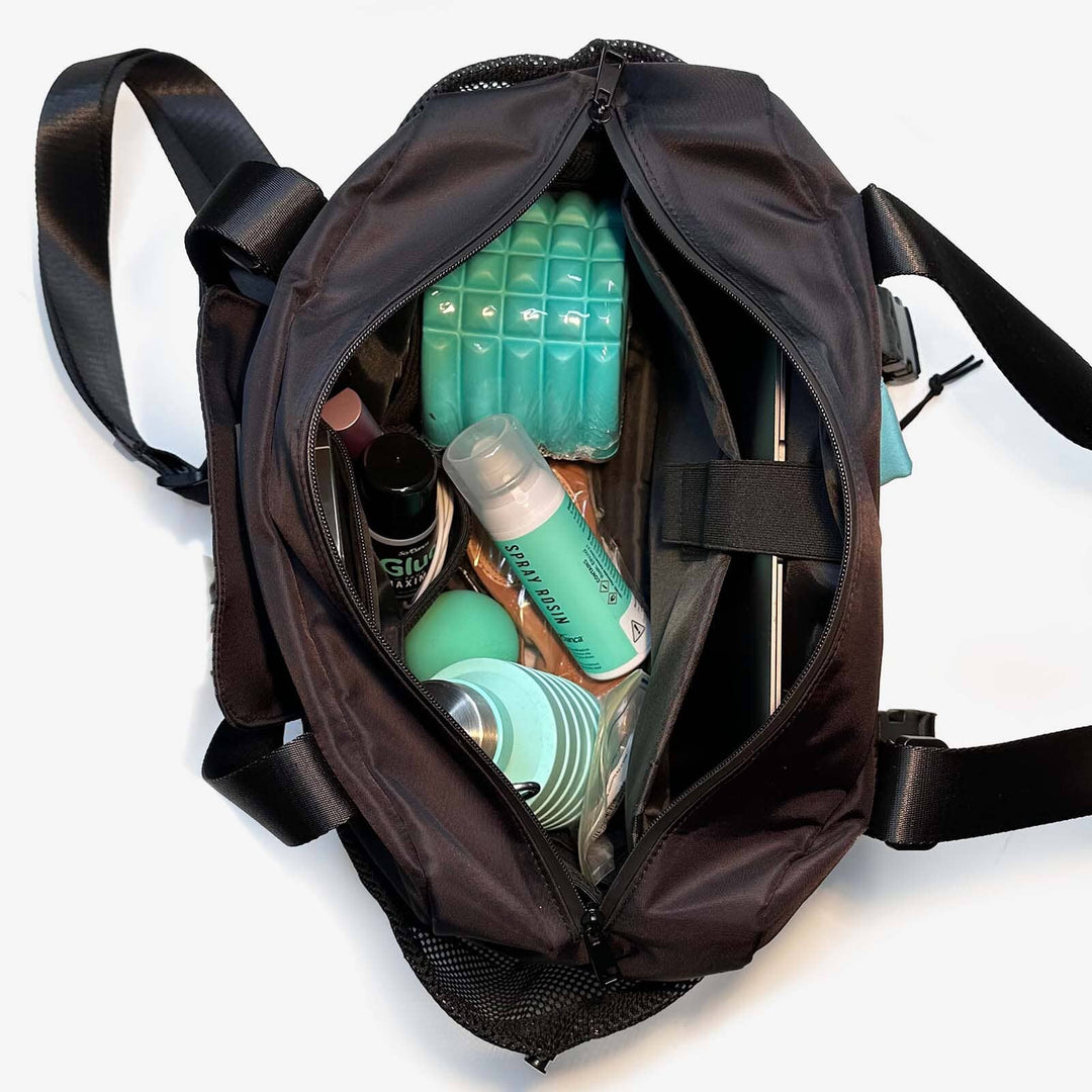 Black backpack with personal care items including bottles and a green block on a white background