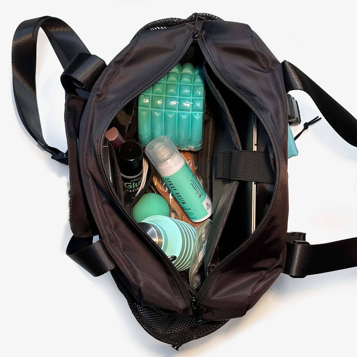 Black backpack with personal care items including bottles and a green block on a white background