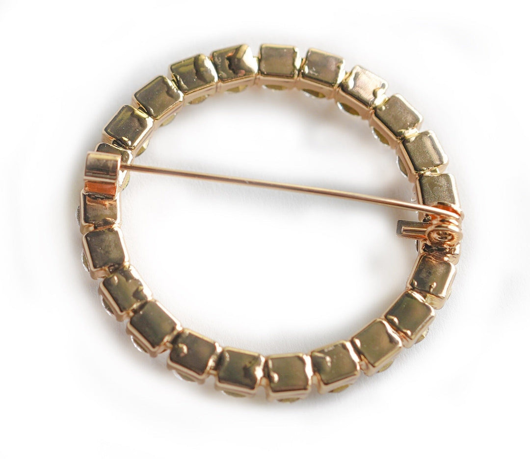 Gold circular brooch with square beads on a white background