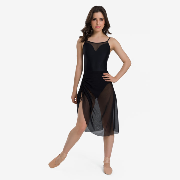 A woman modeling a black dance dress with sheer mesh panels and nude tulle side panels, posed against a light gray studio background.