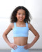 Young girl wearing a light blue sports bra and leggings against a plain background