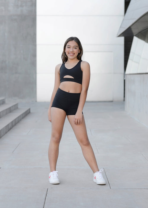 Woman in black athletic wear standing on a concrete surface with a modern building in the background