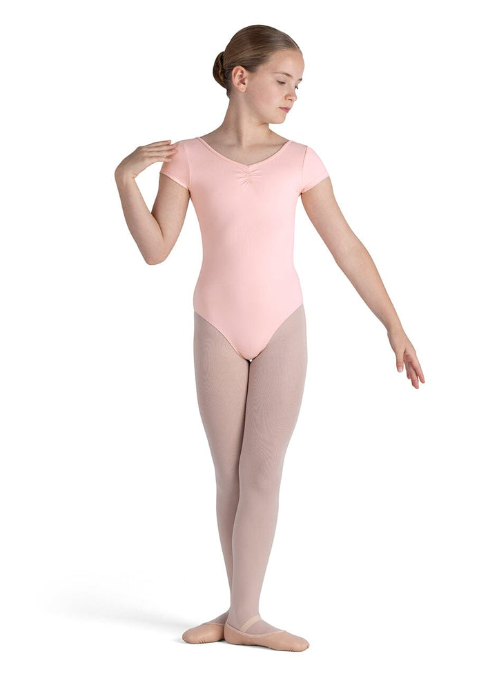 Young girl in a pink leotard and beige tights on a white background