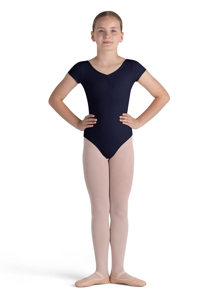 Young girl wearing a navy blue leotard and beige tights on a white background
