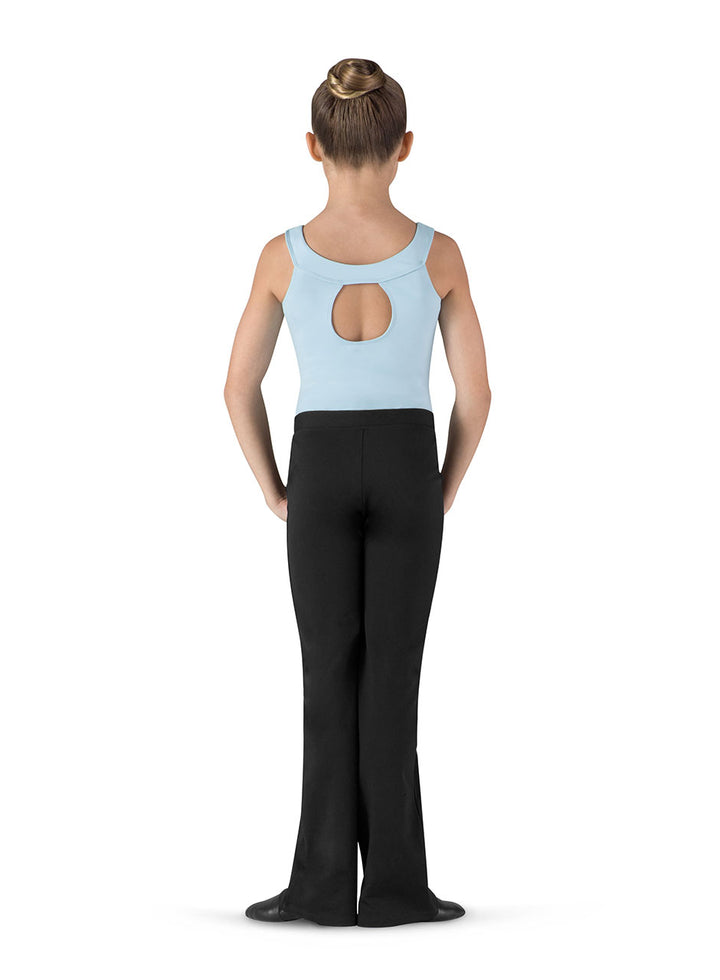 A child dancer shown from the back, wearing a light blue sleeveless leotard with a circular back cutout and black flared dance pants, standing against a plain white background.