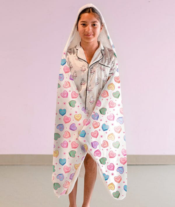 Person wearing a colorful heart-patterned blanket over their shoulders against a plain background