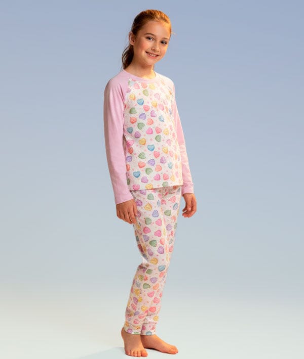 Young girl wearing a pink pajama set with colorful heart patterns on a light blue background