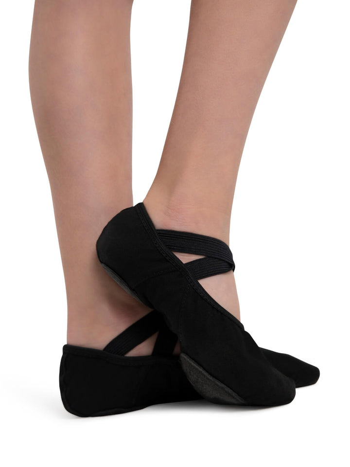 Black ballet shoes worn by a person on a white background