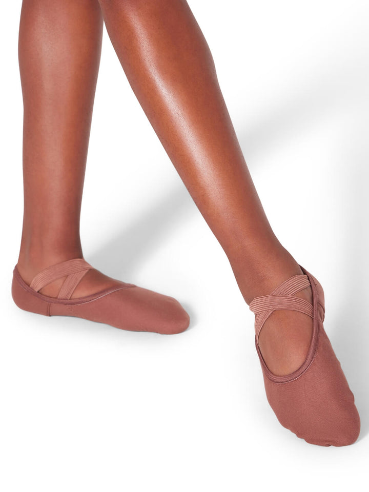 Brown ballet shoes worn with tights on a white background