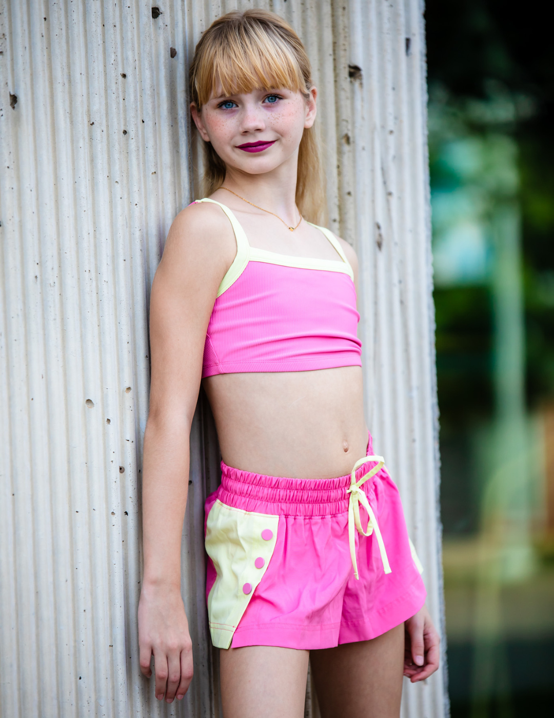 Young girl wearing a pink and yellow swimsuit against a textured wall.