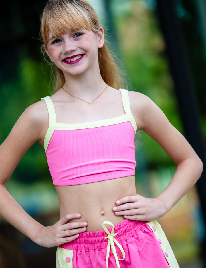 Young girl wearing a pink sports bra and shorts with yellow straps and trim.