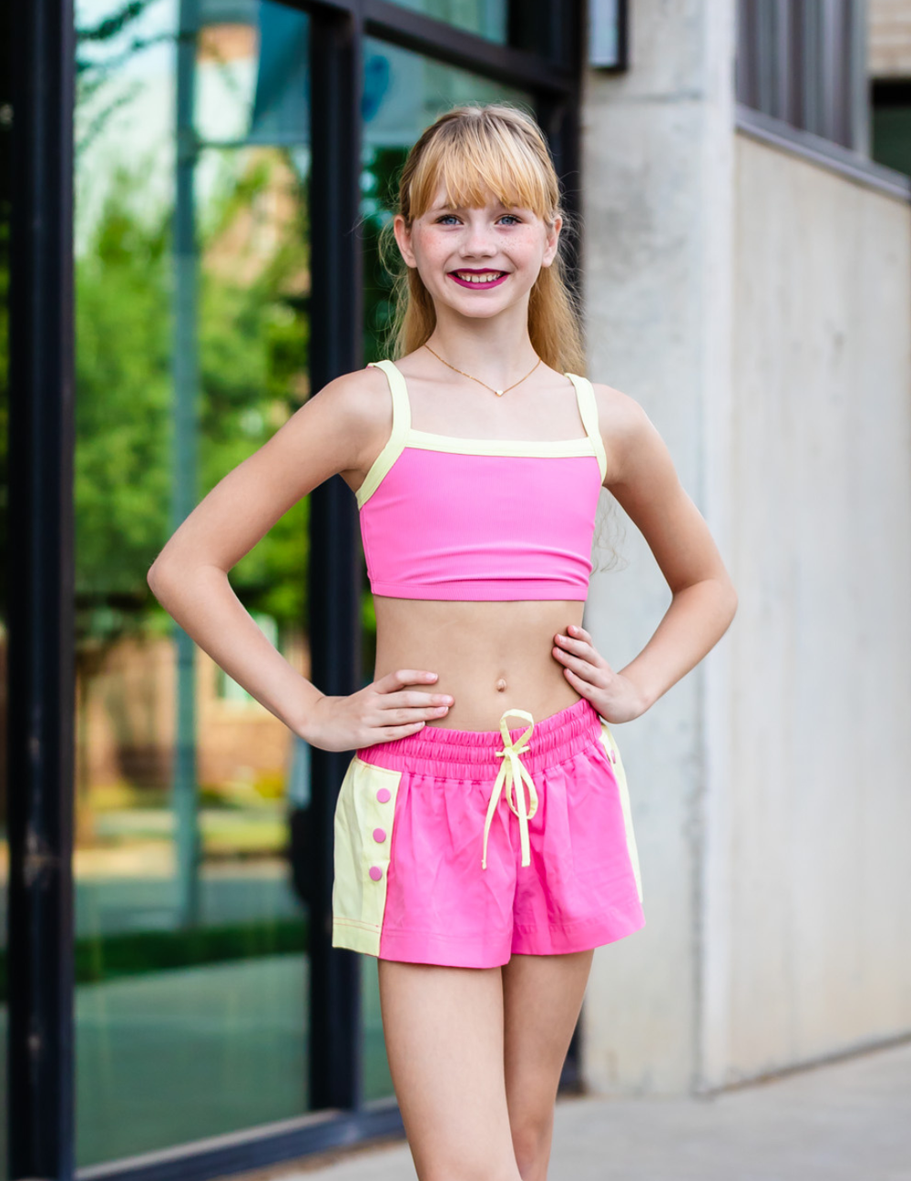 Young girl in a pink and yellow outfit standing outdoors.