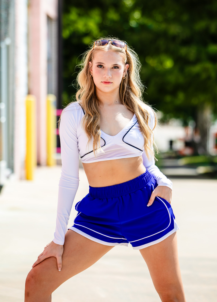 Woman in a white long-sleeve crop top and blue shorts standing outdoors.