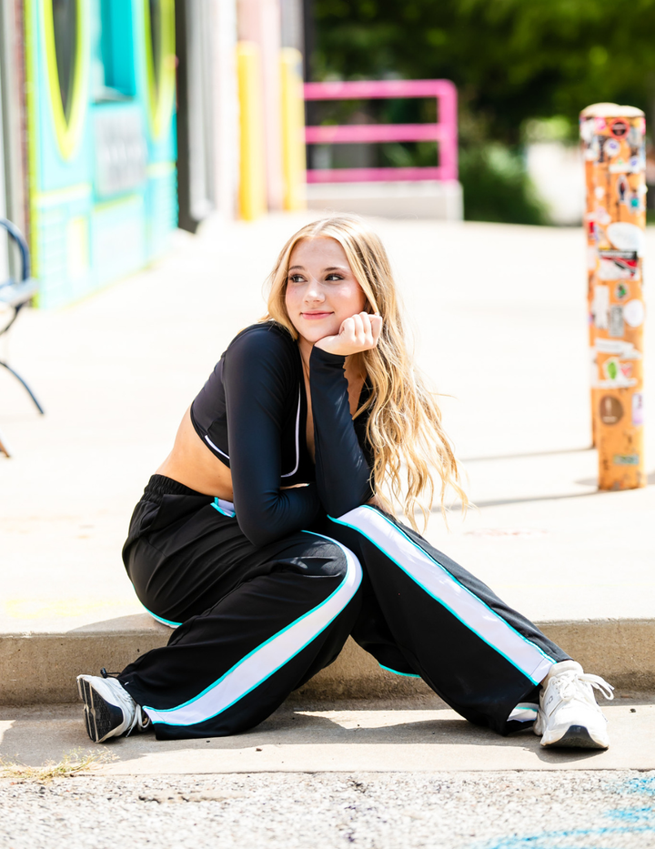 Woman in black tracksuit sitting on a sidewalk with colorful background