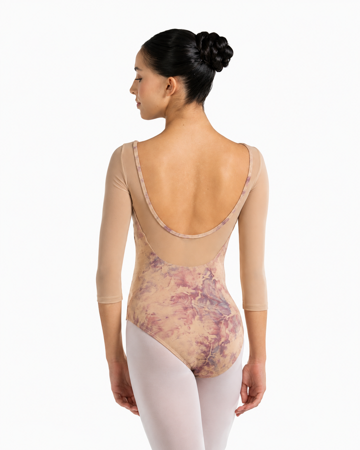 A woman modeling a three-quarter sleeve leotard from the back, showing a dusty pink and purple floral pattern over a nude base, paired with light pink tights against a white background.
