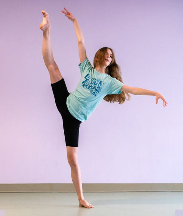 Dancer in a green t-shirt Dancers are the athletes of God and black leggings posing against a light purple wall.