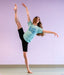 Dancer in a green t-shirt Dancers are the athletes of God and black leggings posing against a light purple wall.