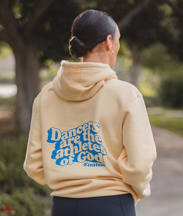 Person wearing a beige hoodie with a blue quote on the back, standing outdoors.