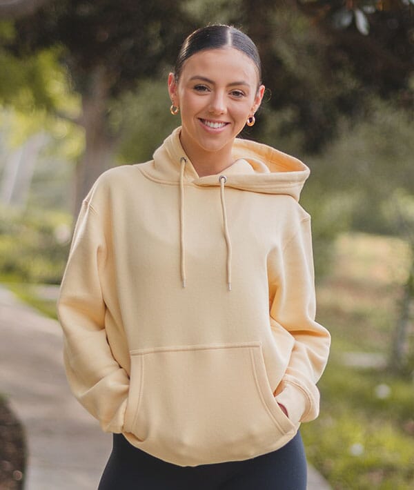 Woman wearing a beige dance hoodie outdoors with greenery in the background