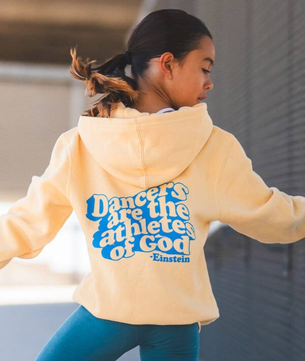 Person wearing a beige hoodie with blue text, standing outdoors.