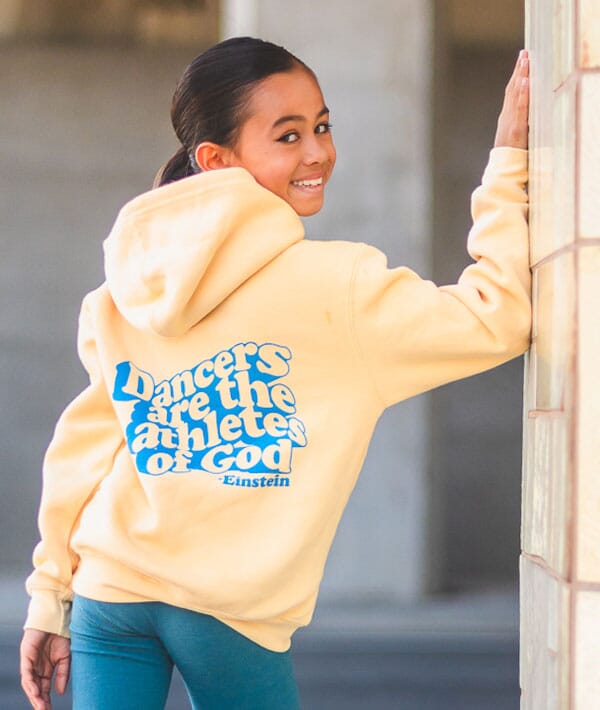 Person wearing a yellow hoodie with text, standing against a neutral background