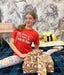 Girl in red shirt with Christmas-themed presents on a floral-patterned wall background