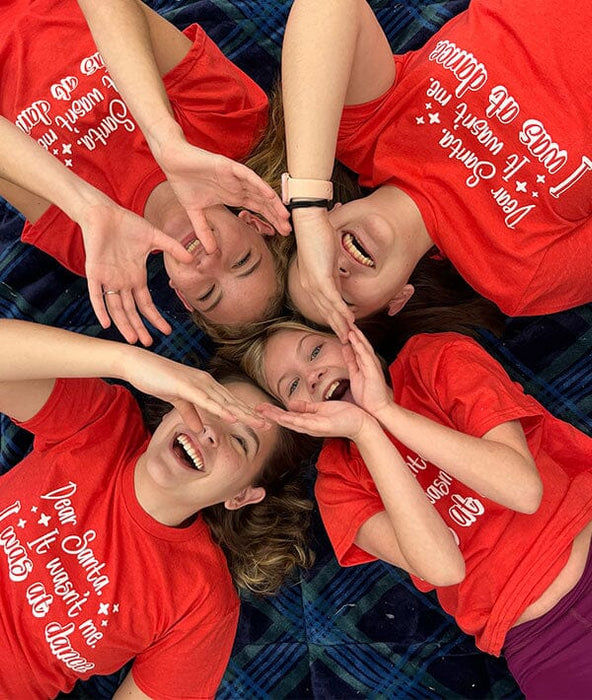 Four people wearing red shirts with white text, forming a circle with their hands.