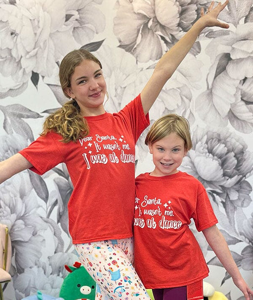 Two children wearing red t-shirts with humorous text against a floral wallpaper background.