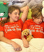 Two children wearing red shirts with humorous text, lying on a bed with stuffed animals.