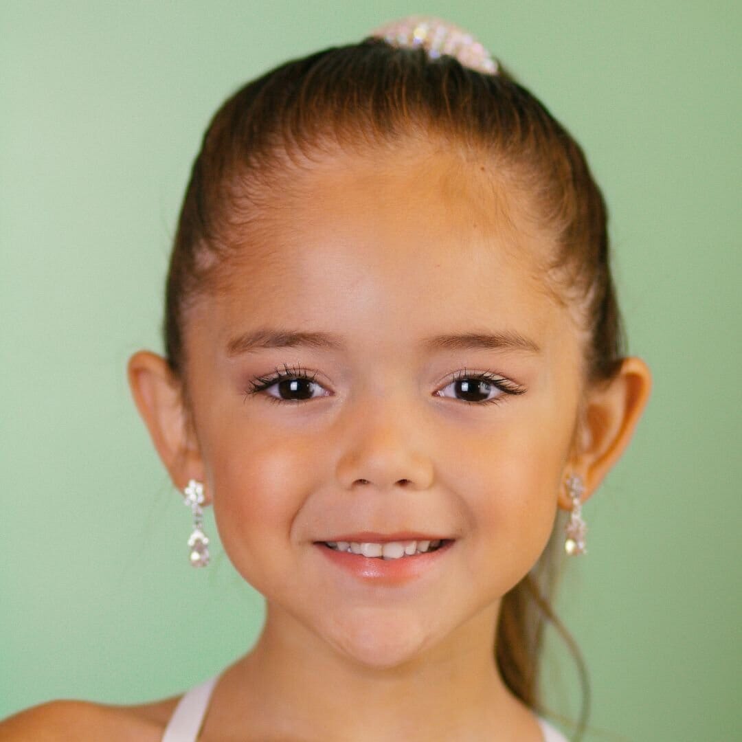 Young girl with a ponytail and earrings against a green background