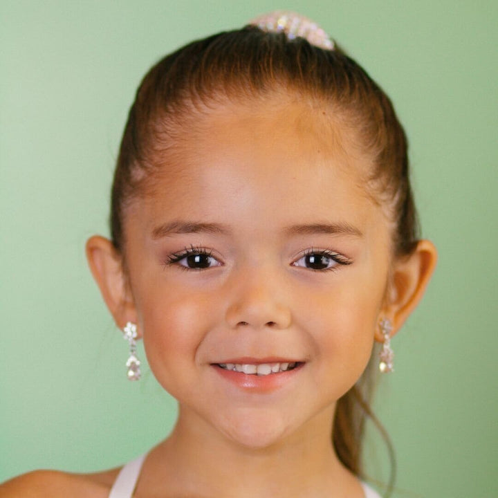 Young girl with a ponytail and earrings against a green background