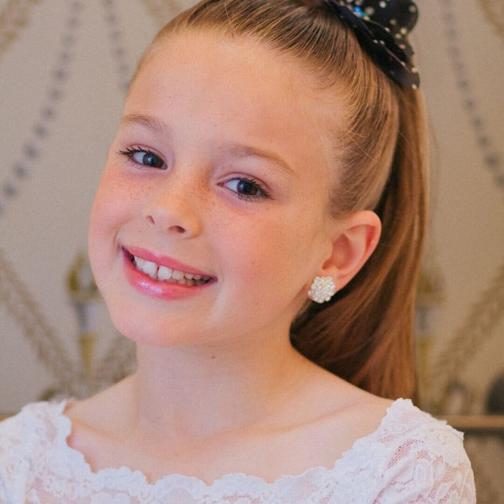 Young girl with a ponytail wearing a white lace top indoors.