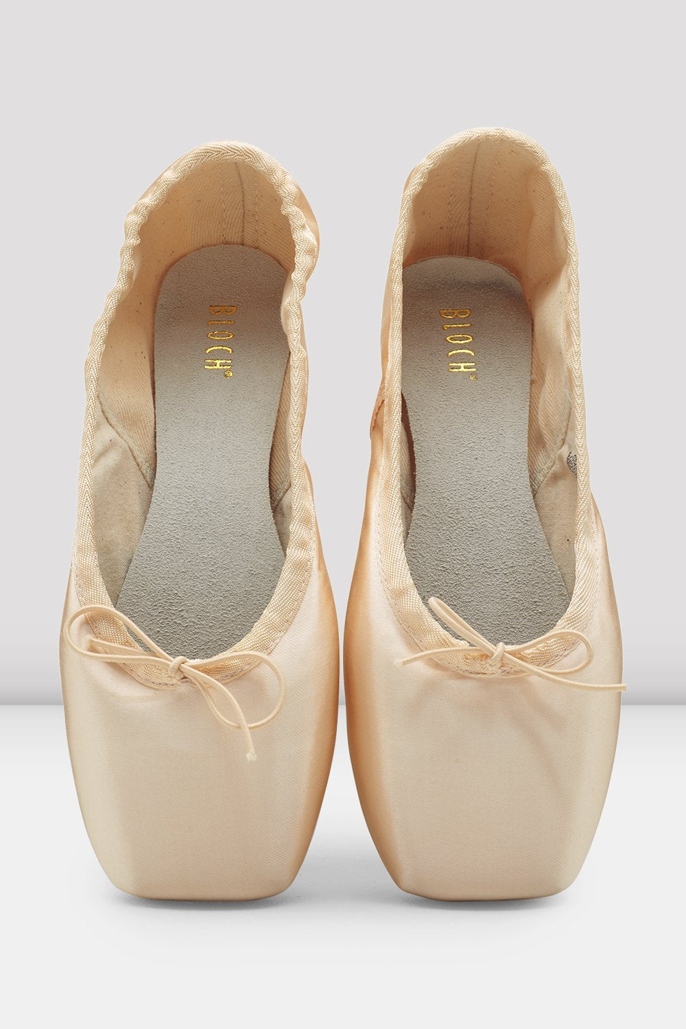 Pair of beige ballet shoes with ribbons on a light gray background