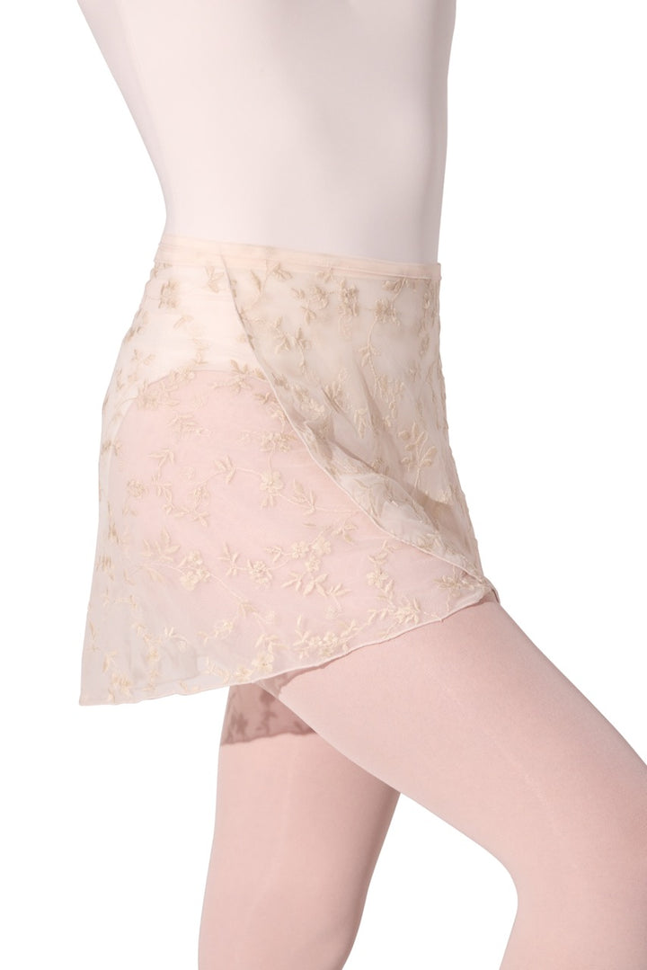 A close-up of a model wearing a sheer nude mesh skirt with gold floral embroidery, paired with matching nude tights against a white background.
