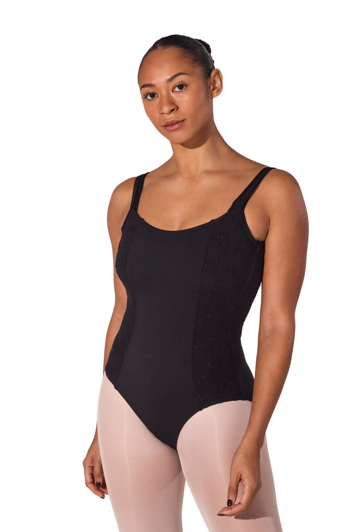 A female dancer wearing a black bodysuit with textured side panels and light pink tights, standing against a solid white background.