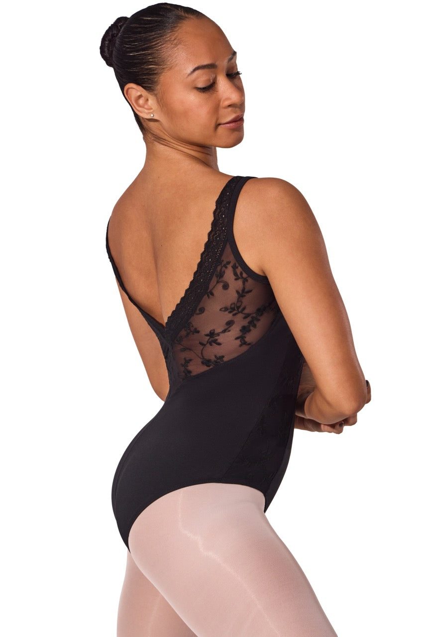A woman modeling a black lace-trimmed dance leotard from the back, paired with sheer nude tights, against a solid white background.