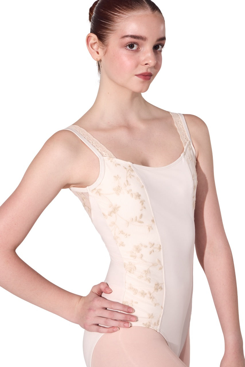 A young female dancer wearing a light beige bodysuit with sheer floral lace panels on the sides, posed against a solid white background.
